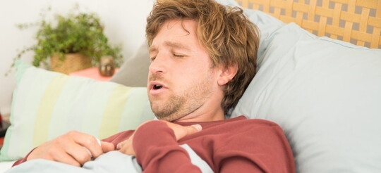 Ein Mann liegt mit Gliederschmerzen aufgrund einer Erkältung im Bett.