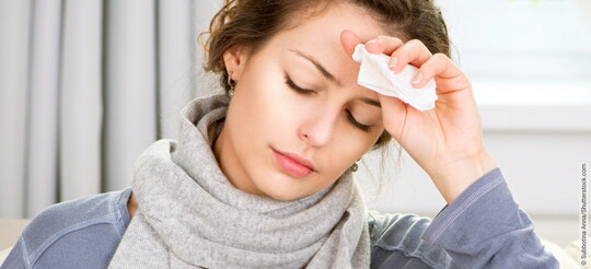 Eine Frau, die erkältet ist, hält sich die Stirn, da sie unter Fieber leidet.