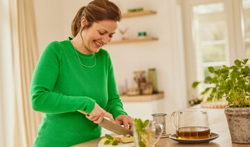 Lächelnde Frau in der Küche schneidet Ingwer und bereitet ein gesundes Getränk mit Minze zu