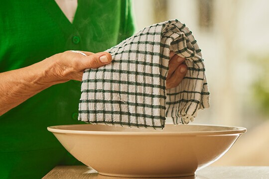 Frau beim Tauchen eines Handtuchs in warmes Wasser, um Wadenwickel als Hausmittel gegen Erkältung anzuwenden.